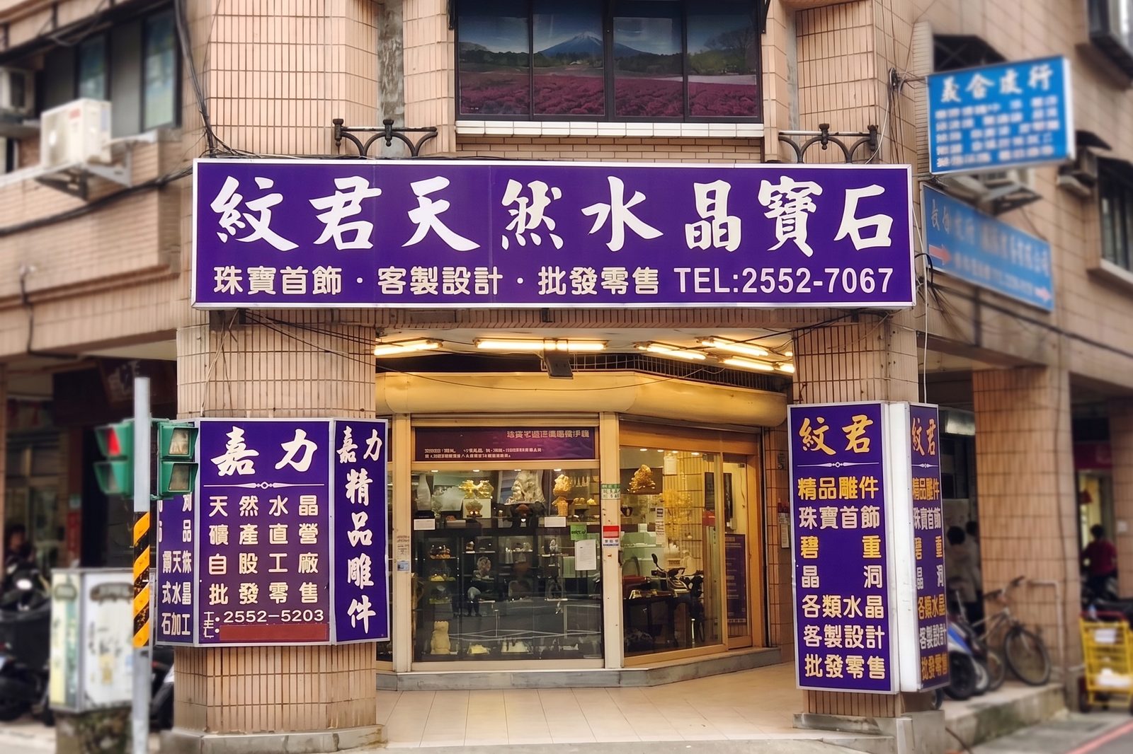 紋君堡石坊門市外觀,紫色招牌寫著「紋君天然水晶寶石 珠寶首飾・客製設計・批發零售 TEL:2552-7067」,位於台北大同區長安西路街角