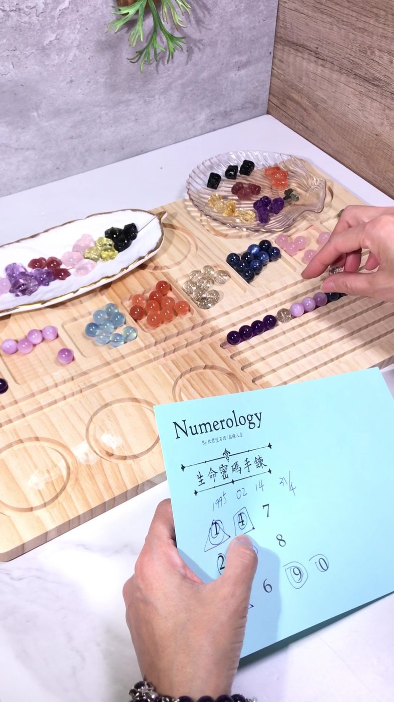 紋君老師手持填好的 Numerology 卡，桌上是待挑選的水晶珠盤