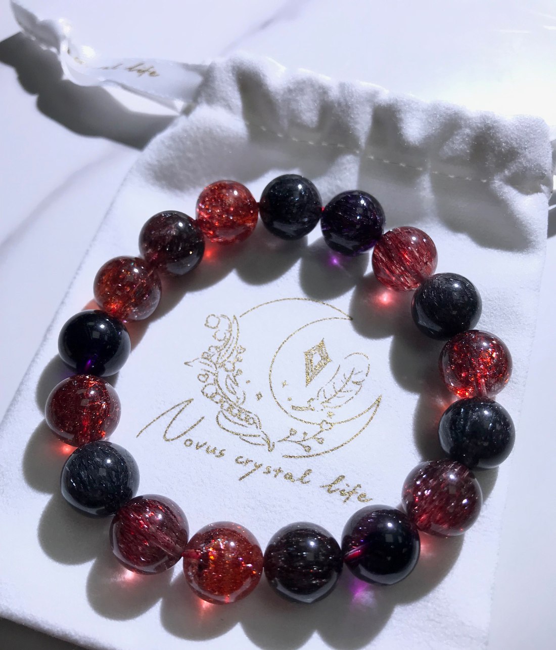 燙金 logo 的白色絨布晶品袋,上面放著一條紫髮晶手鍊